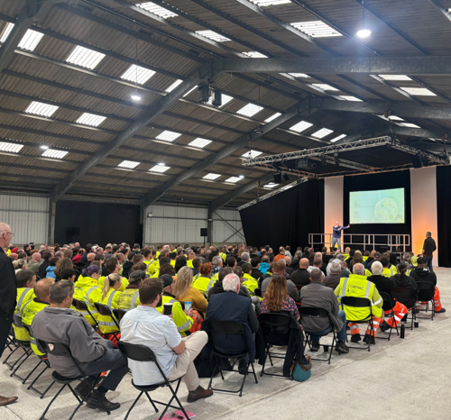 A mixture of people wearing high-vis jackets and regular clothes listening attentively to presentation