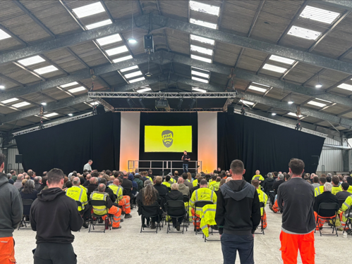 Cormac workers attend event, sitting on chairs inside warehouse