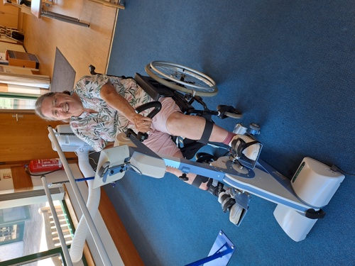 A wheelchair users sits at an adaptive exercise bike with a big grin on her face