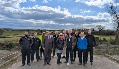 A group of people from Cormac stand with business professionals in front of a green field