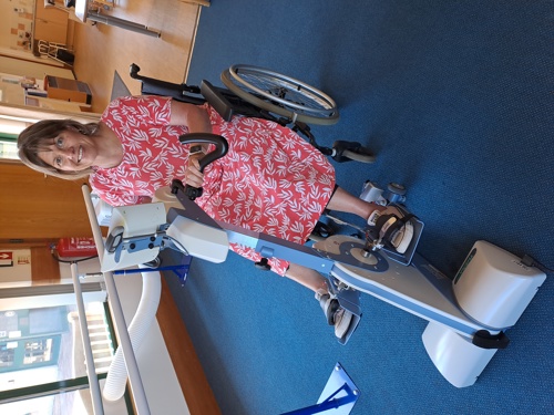 A smiling lady in a brightly coloured dress sitting on an adaptive exercise bike